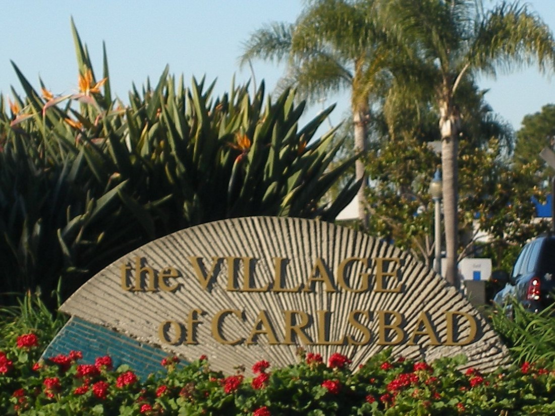 The landmark &lsquo;Village of Carlsbad&rsquo; sign surrounded by palm trees and flowers